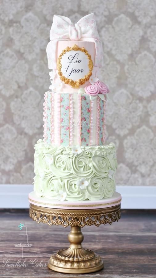 a three tiered cake with pink and green frosting on top, sitting on a gold pedestal