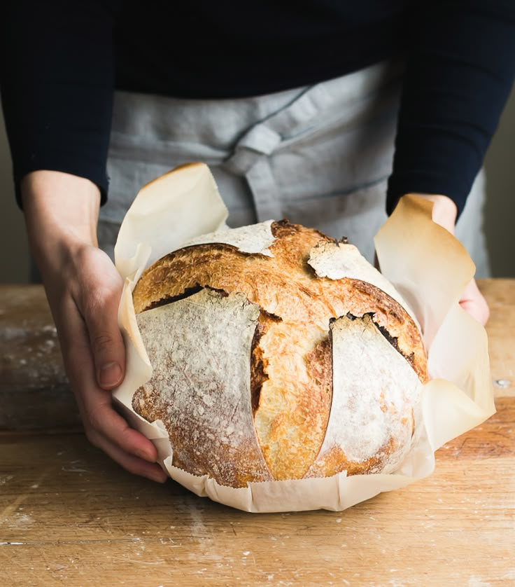 a person holding a loaf of bread on top of a wooden table