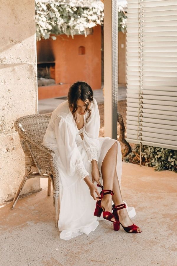 a woman is sitting on a chair and tying her red high heeled shoes with one hand