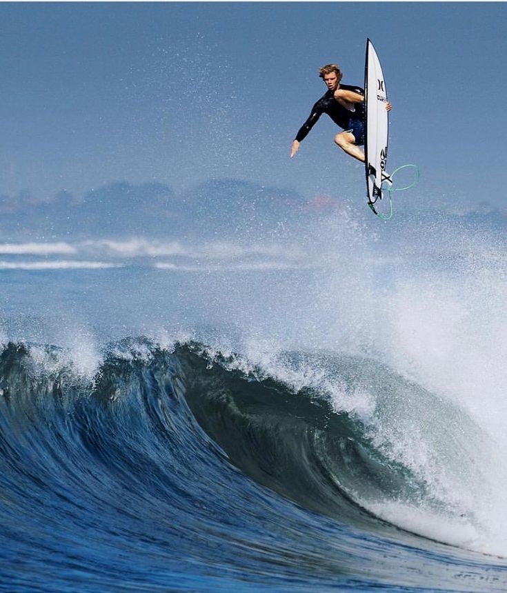 a man flying through the air while riding a surfboard on top of a wave