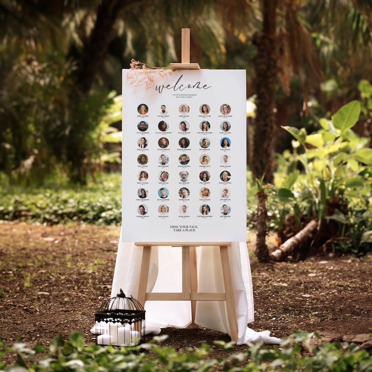 an easel with pictures on it sitting in the grass near some trees and bushes