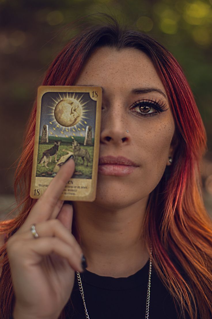 a woman with red hair holding up a tarot card in front of her face