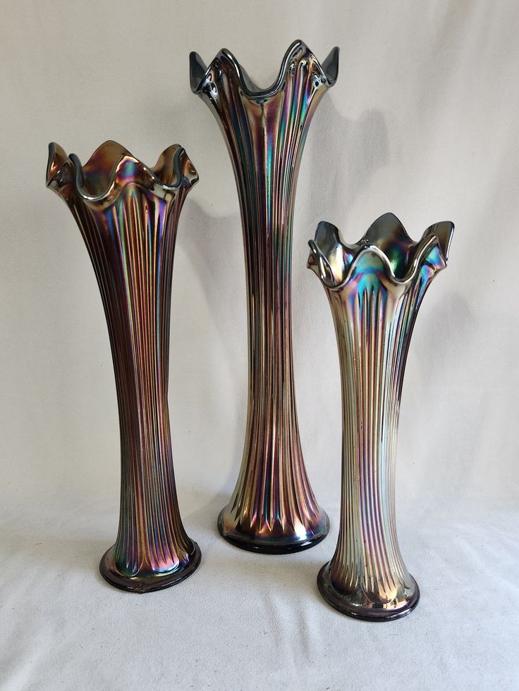 three metallic vases sitting next to each other on a white surface