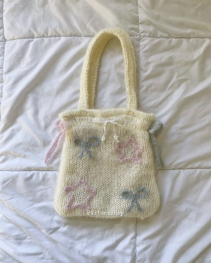 a white bag with pink and blue flowers on it sitting on a bed next to a pillow