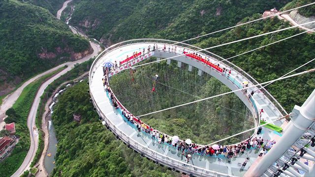 people are walking on the glass walkway above the valley and mountains in this aerial view