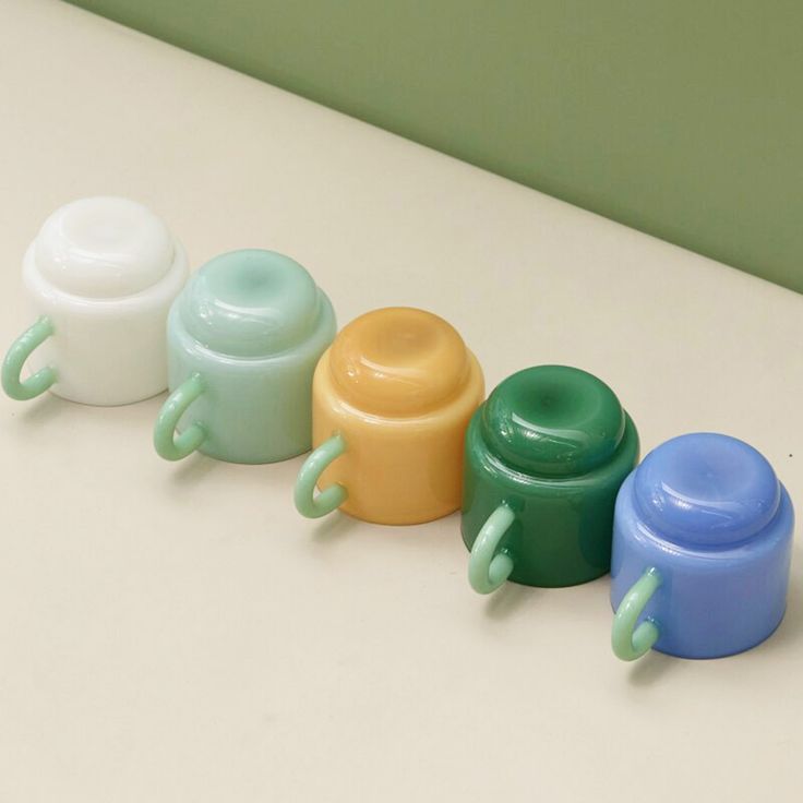 four baby bottles lined up next to each other on a white counter top with green, blue, and yellow handles