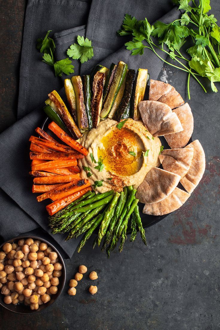 a platter with carrots, asparagus and hummus next to other foods