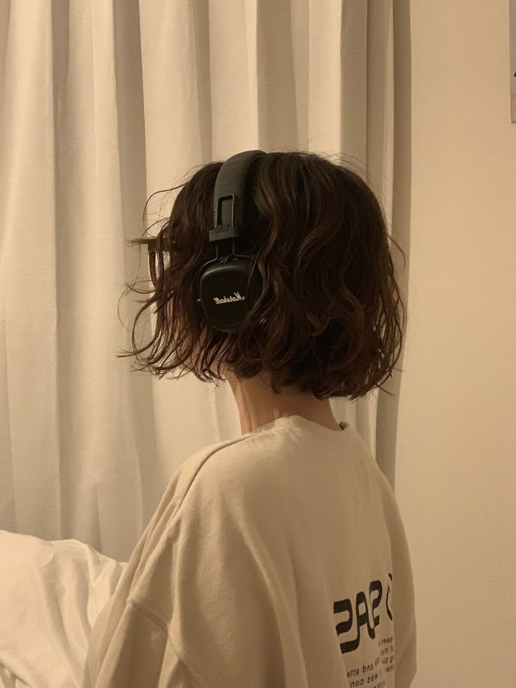 a person with headphones on their ears standing in front of a bed and looking out the window