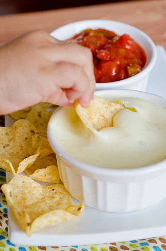 a person dipping tortilla chips into a small white bowl filled with dip and salsa