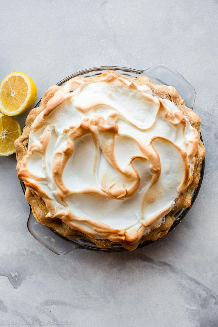 a lemon meringue pie sitting on top of a table next to a slice of lemon