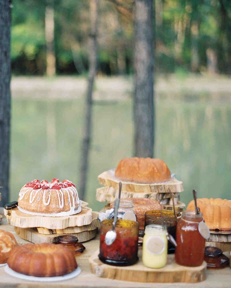 an outdoor picnic table with cakes, jams and bundt cake on wooden boards