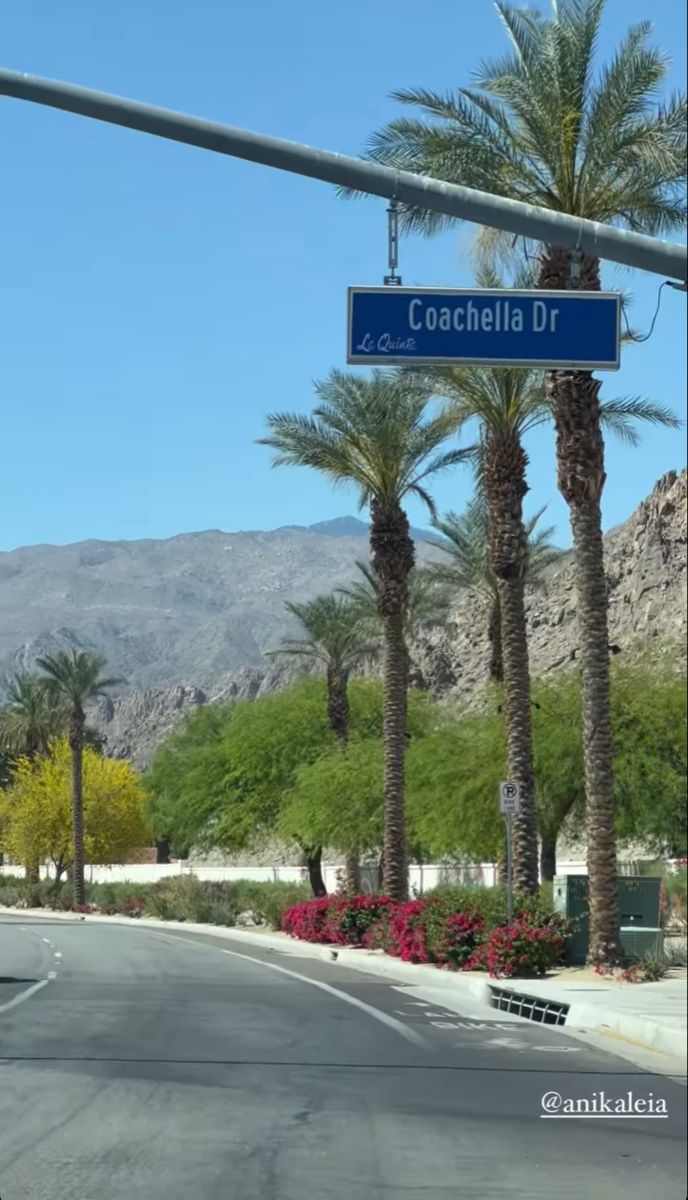 a street sign on the side of a road with palm trees and mountains in the background