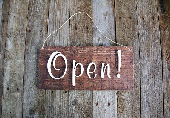 a wooden sign that says open hanging on a wood planked wall with string attached to it