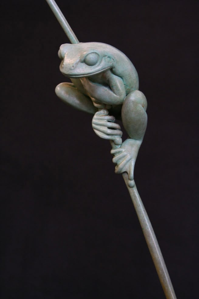 a statue of a frog sitting on top of a stick