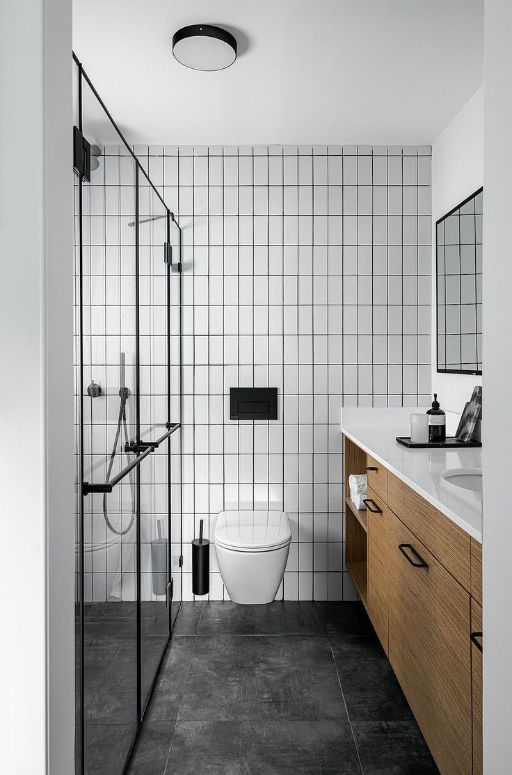 a white toilet sitting next to a walk in shower under a bathroom mirror on top of a wooden cabinet