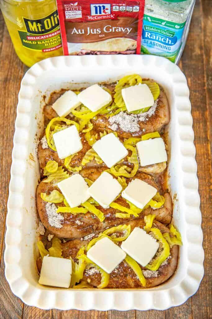 a casserole dish with cheese and onions in it on a wooden table next to two bottles of mustard