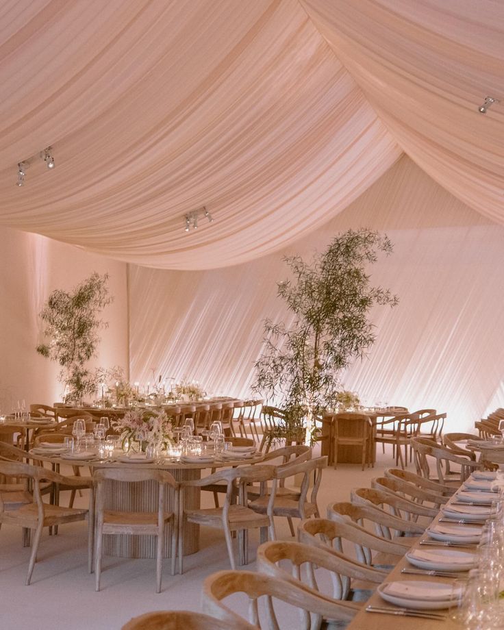 a banquet hall with tables and chairs covered in white draping, decorated with greenery