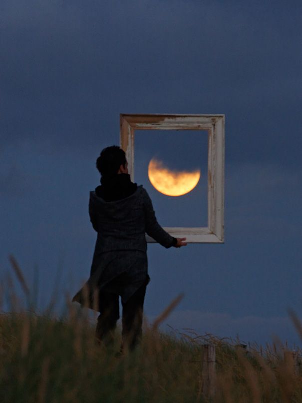 a person standing on top of a grass covered hill next to a window with the moon in it