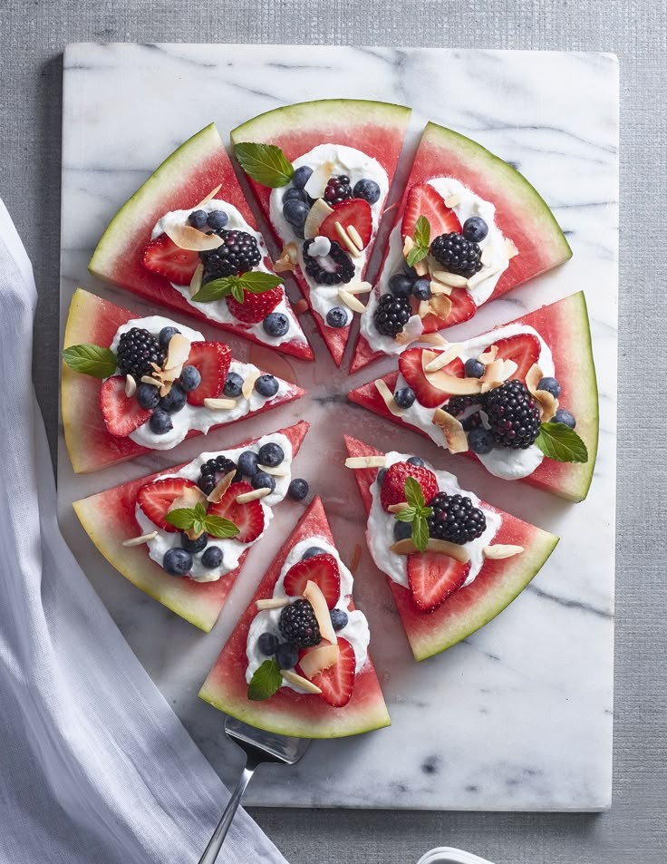 slices of watermelon and berries arranged on a marble platter with utensils