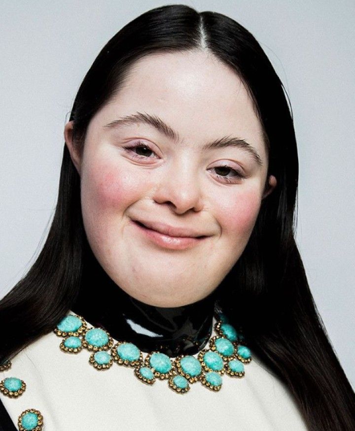 a woman with long black hair wearing a white top and turquoise jeweled collar smiling at the camera