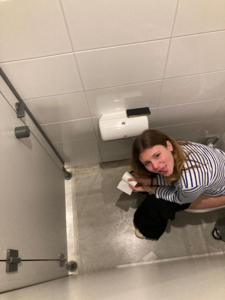 a woman sitting on the floor in front of a toilet paper dispenser