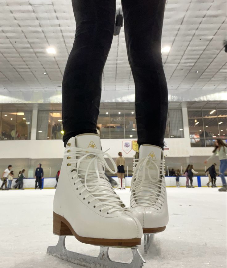 a pair of white ice skates sitting on top of an ice rink with people in the background