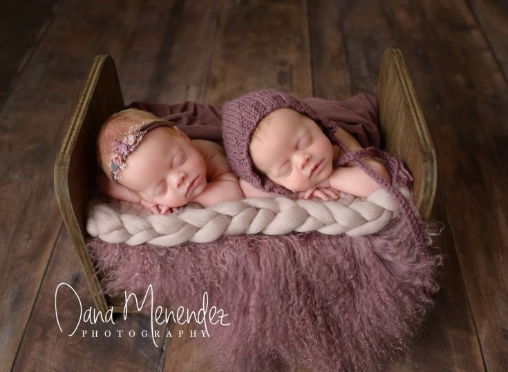 two newborn babies are sleeping in a wooden crate on a wood floor, wearing knitted bonnets