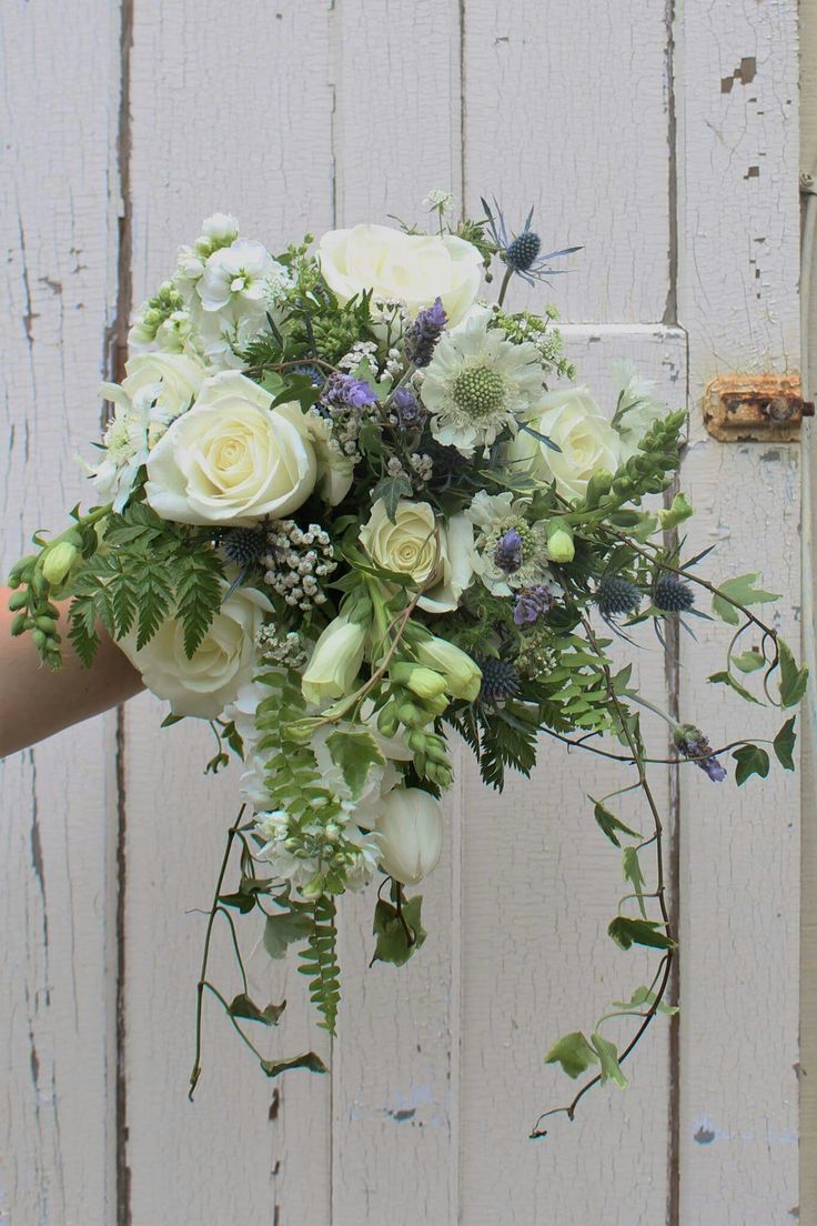 a bouquet of flowers is held up against a white wooden wall with peeling paint on it