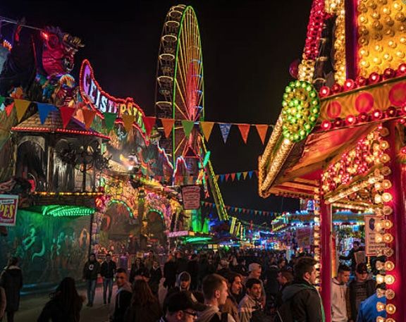 an amusement park at night filled with lots of people and lights on the carnival rides