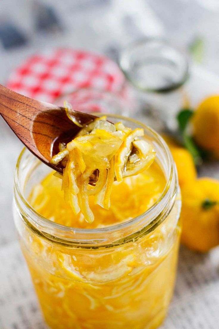 a wooden spoon is holding some food in a jar with lemons and other fruit around it