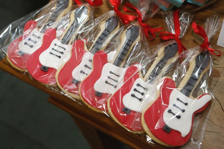 decorated cookies in the shape of guitars are displayed on a table with red ribbon and bows