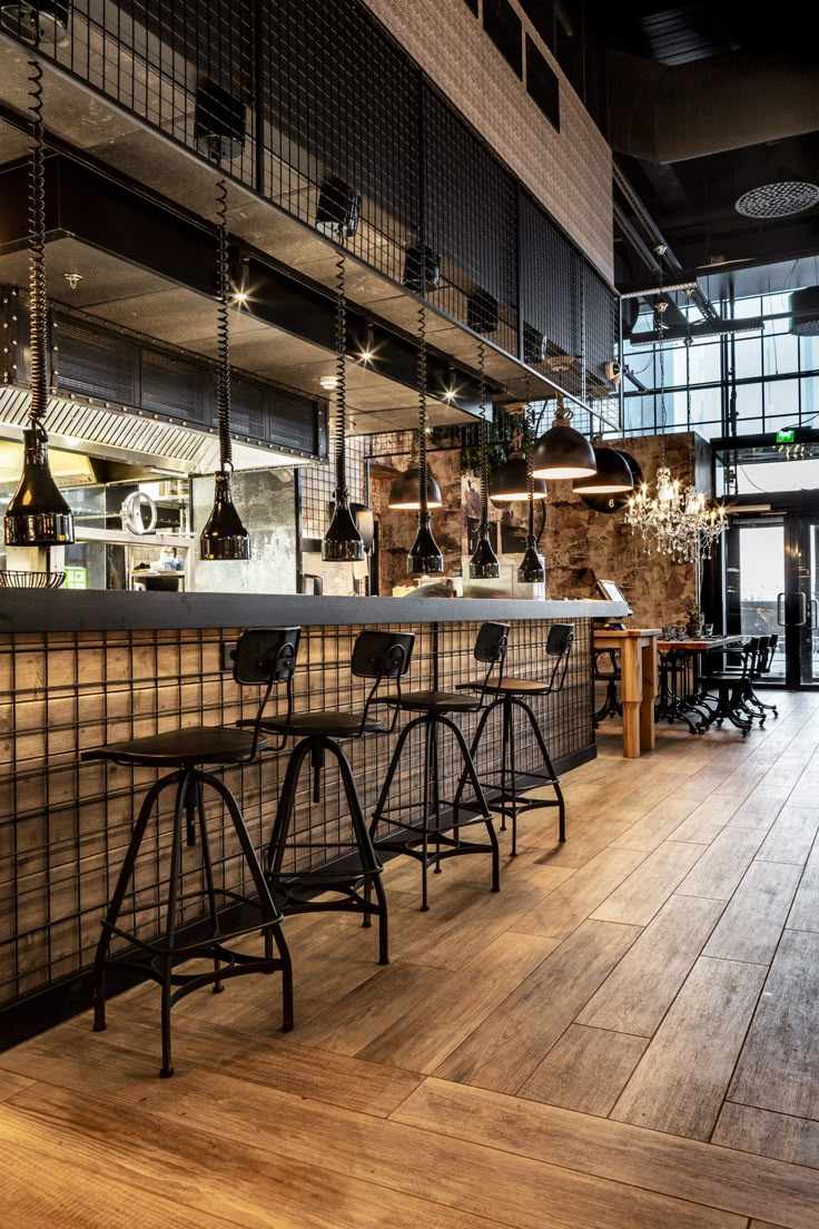 an empty restaurant with bar stools and wooden flooring in the foreground, lights hanging from the ceiling