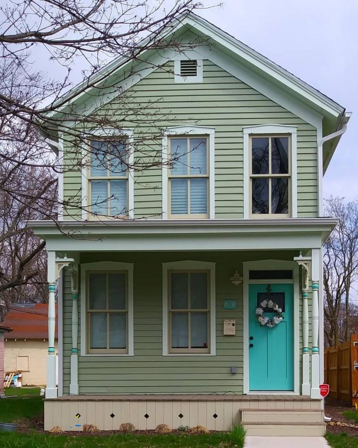 a green house with a blue front door and clock on it's side porch