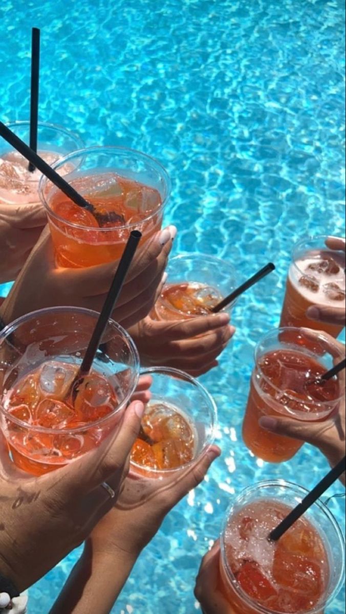 many people are holding up drinks in front of a swimming pool with straws on the rim