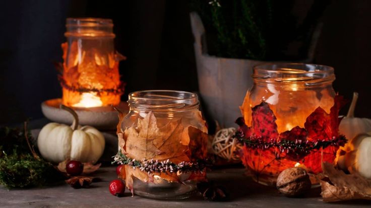 three jars filled with candles sitting on top of a table next to small pumpkins