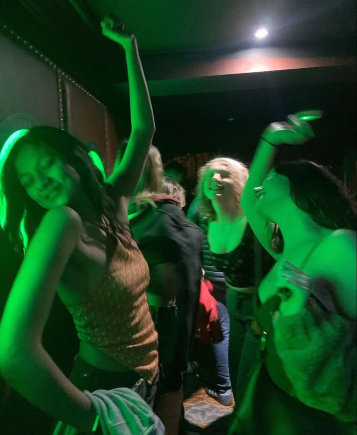 a group of young people dancing in a dark room with green light on the walls