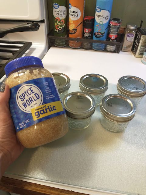 a hand holding a jar of garlic on top of a counter next to other spices