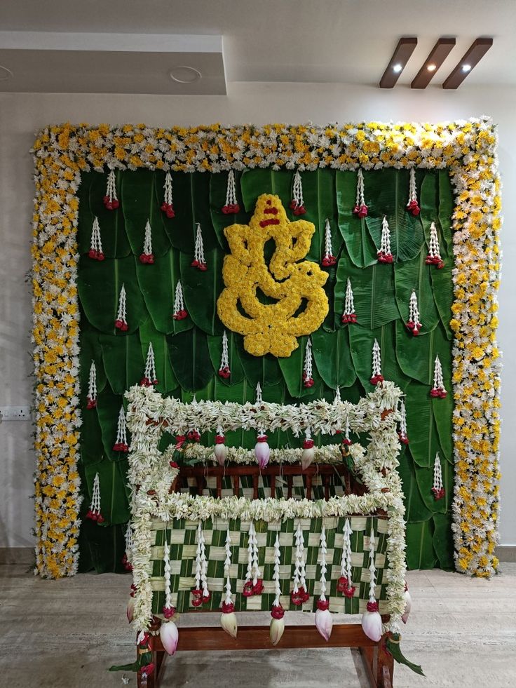 a wall decorated with flowers and a decorative ganeshi idol in the middle, surrounded by greenery