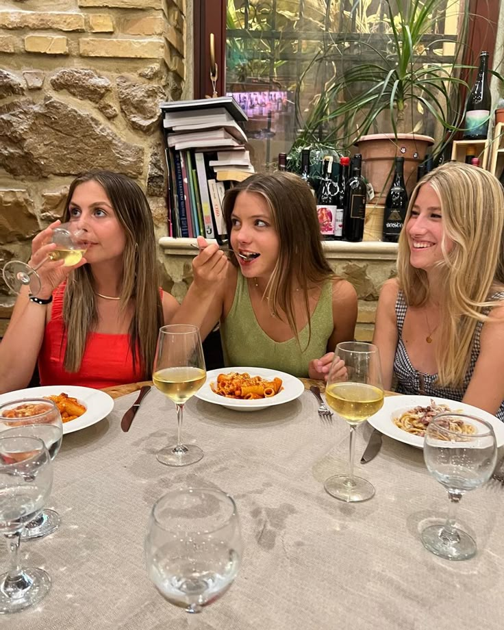 three women sitting at a table eating and drinking wine