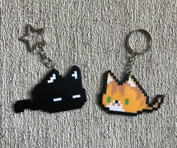 two pixel keychains are laying on the floor, one has an orange and black cat