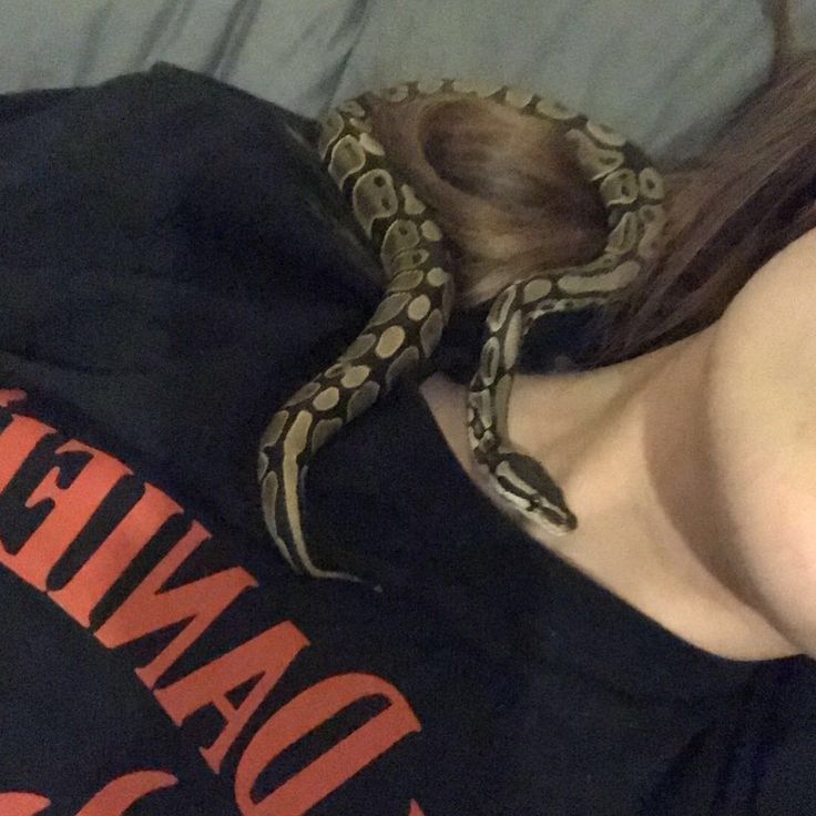 a woman laying on top of a bed with a snake wrapped around her neck and head