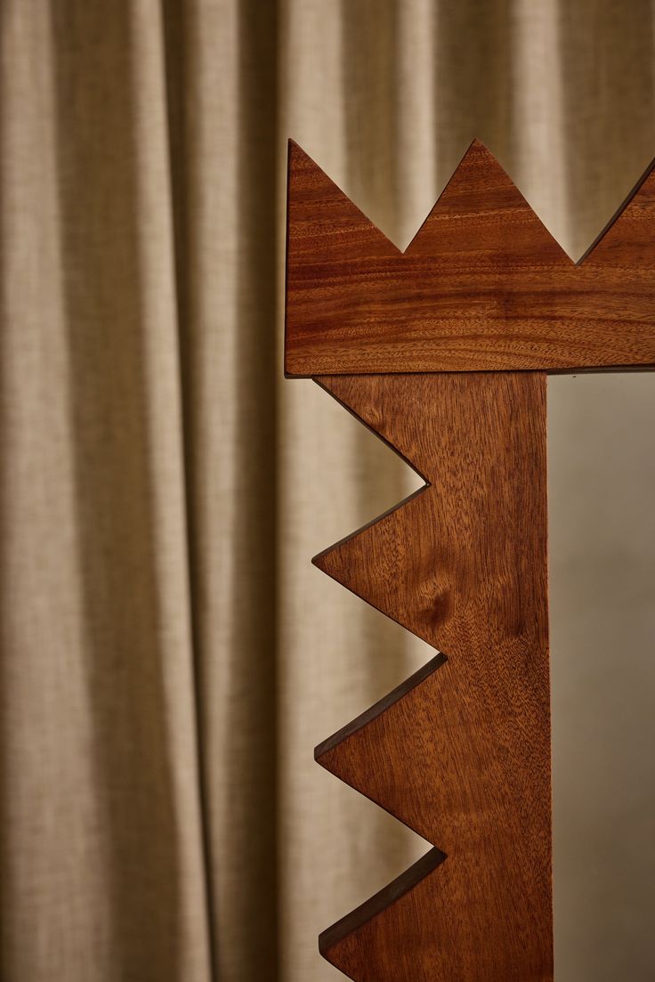 a wooden mirror with an arrow shaped design on the front and back side, hanging from a curtain