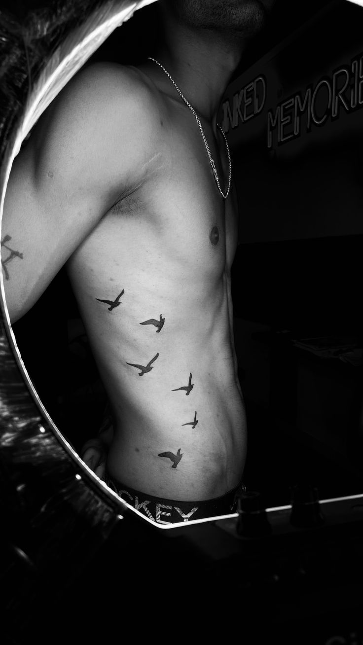 a man with birds on his chest is reflected in a mirror that shows the reflection of another person's shirtless torso