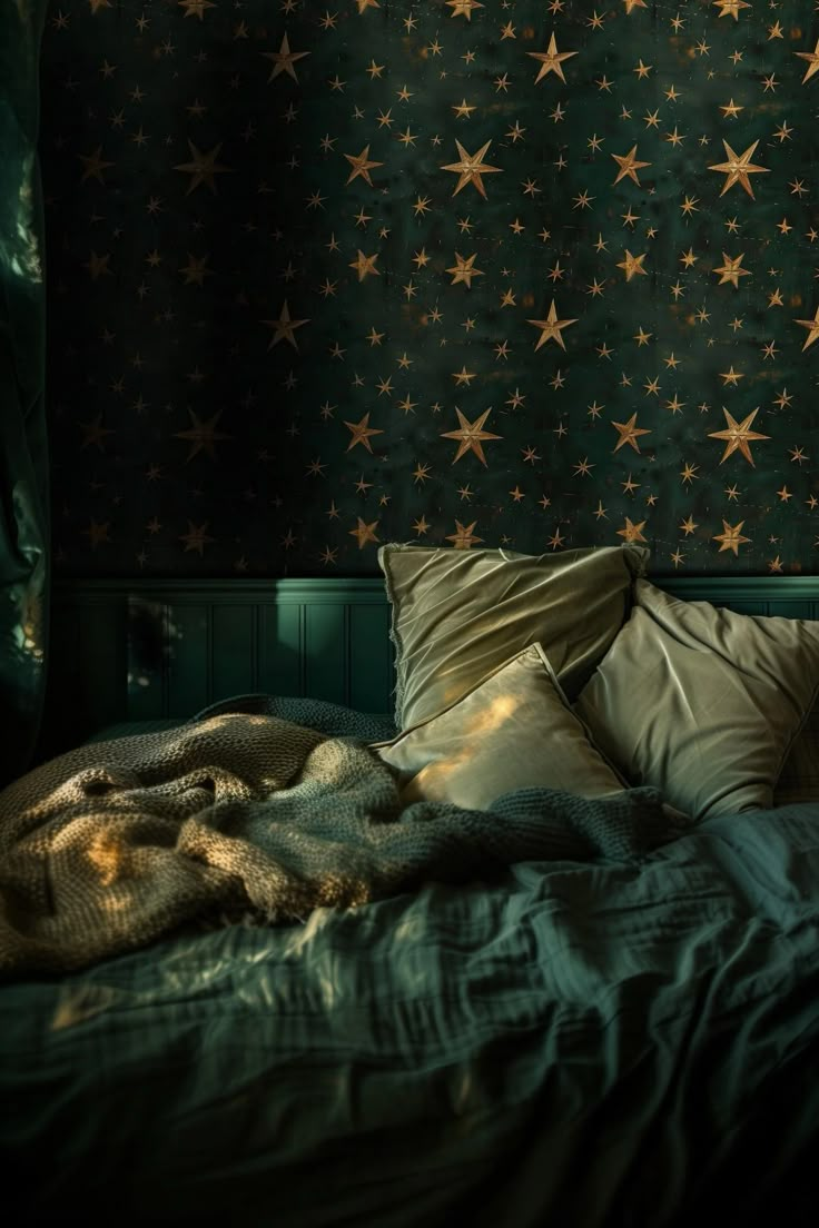 an unmade bed with green sheets and gold stars on the wall behind it in a dark room