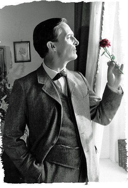 a man in a suit and tie holding a rose up to his face while standing next to a window