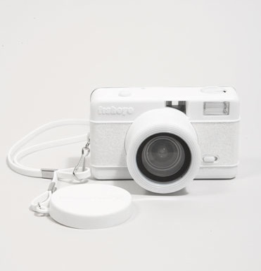 a white camera sitting next to a charger on a white surface with a cord