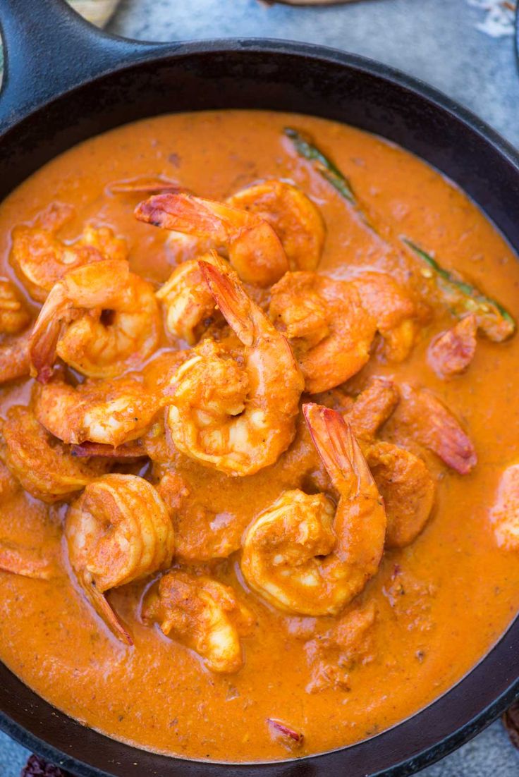 a skillet filled with shrimp and sauce on top of a blue tablecloth next to bread