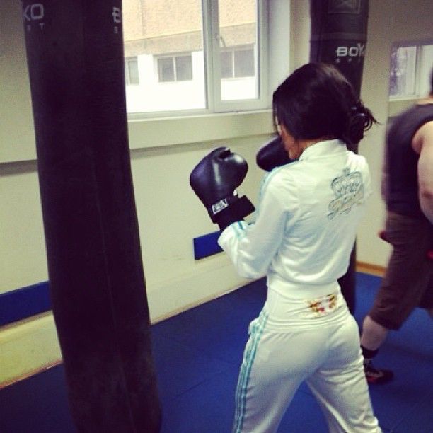 a woman in white boxing outfit standing next to a punching bag with other people behind her