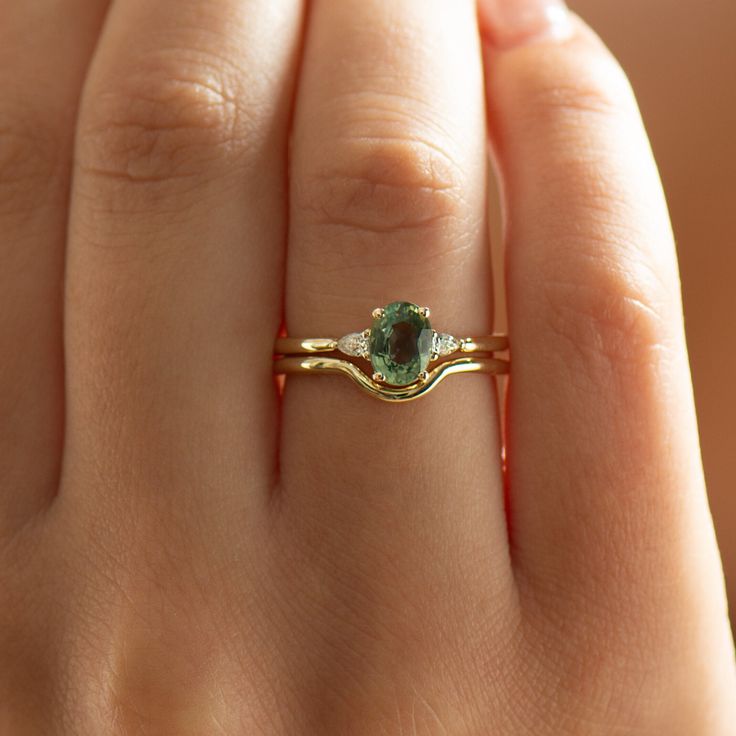 a woman's hand holding a ring with a green stone on top of it