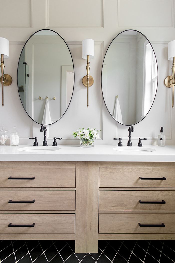 two round mirrors are above the double sinks in this bathroom with black and white tile flooring